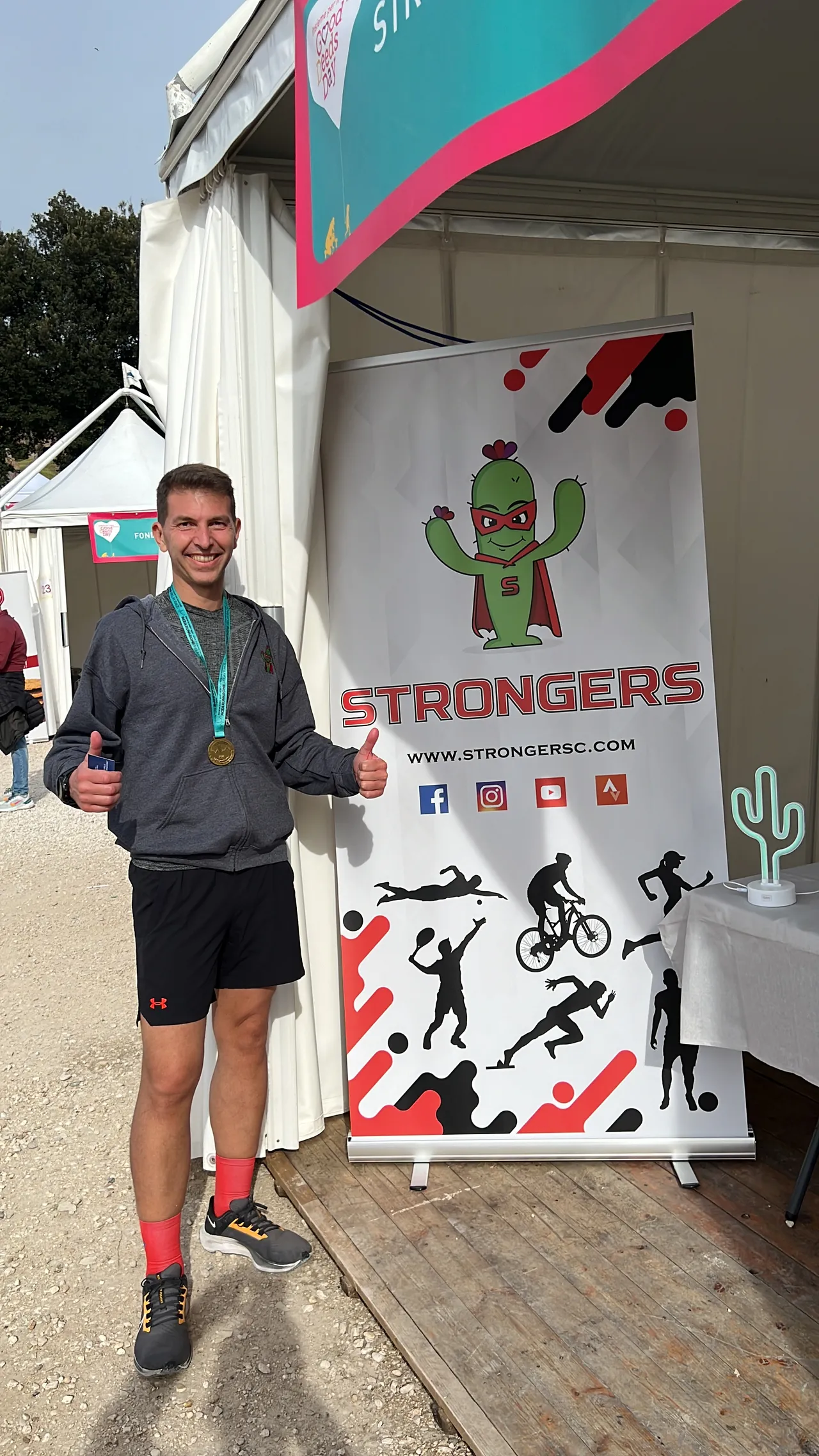 Uno staffettista Strongers con la medaglia davanti al roll-up dello stand