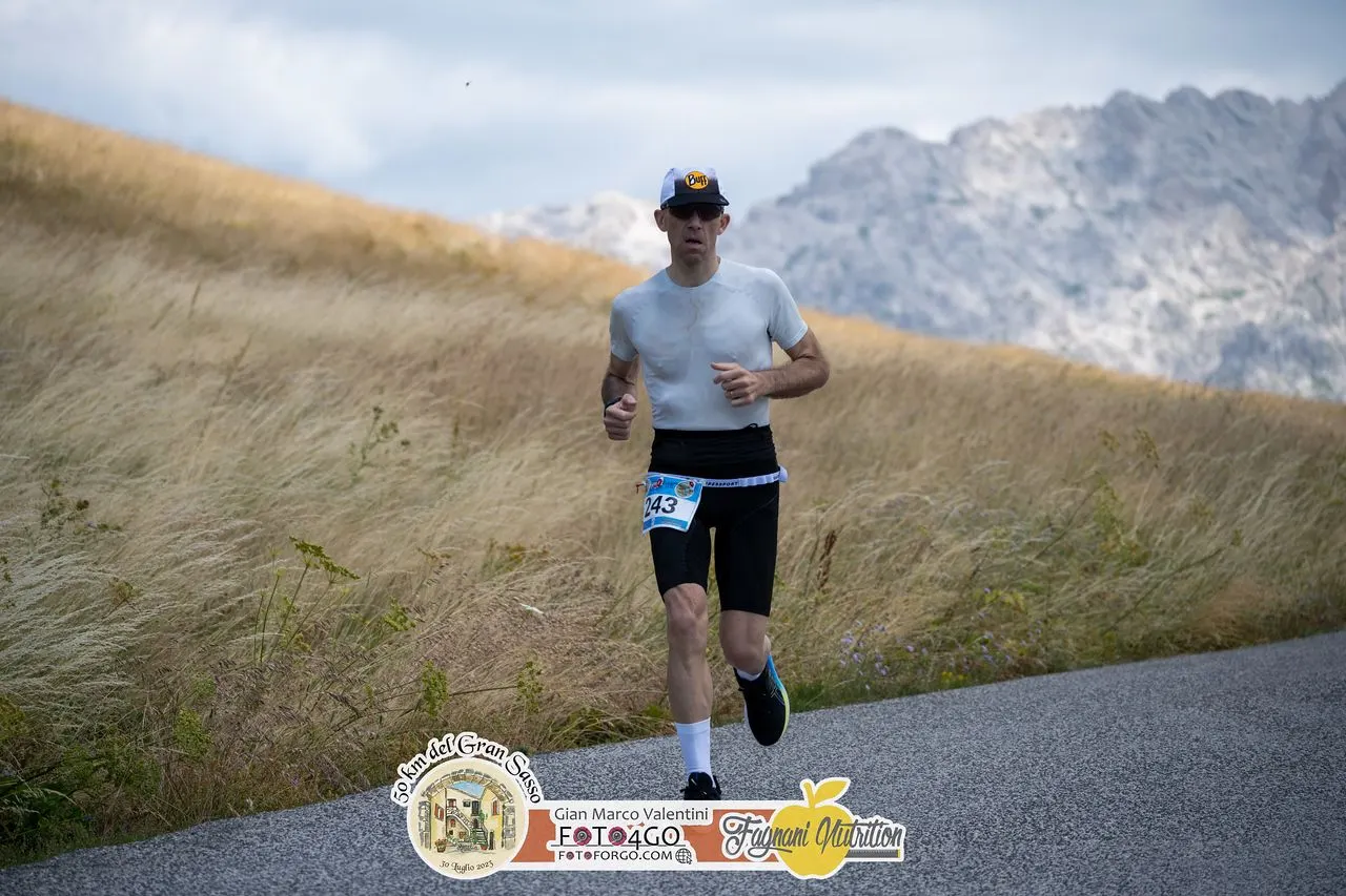 Raffaele corre sulla strada dell'altopiano, con le montagne del Gran Sasso sullo sfondo