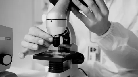 Giovane ricercatrice al microscopio in laboratorio oncologico, simbolo della precision oncology sul cancro al polmone