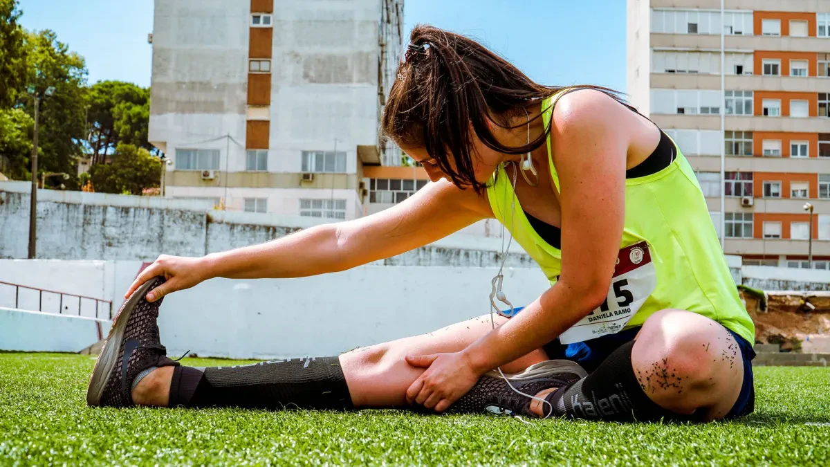 Atleta che si tiene il ginocchio dopo un salto, con espressione di dolore, durante un allenamento outdoor